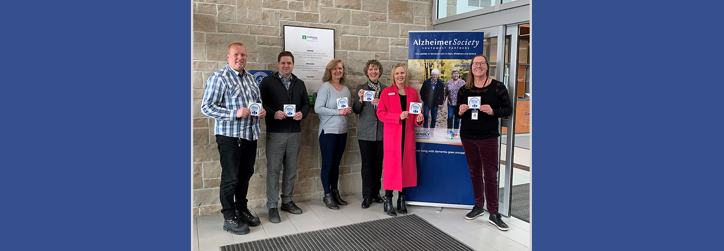 Justin Fidler, Lise Massen, Sean Hanlon and Mayor Aina DeViet of Middlesex Centre, and Leslie Rand and Susan Oster from the Alzheimer Society Southwest Partners, hold the new Dementia Friendly Community Supporter decals that will be going up at municipal buildings.
