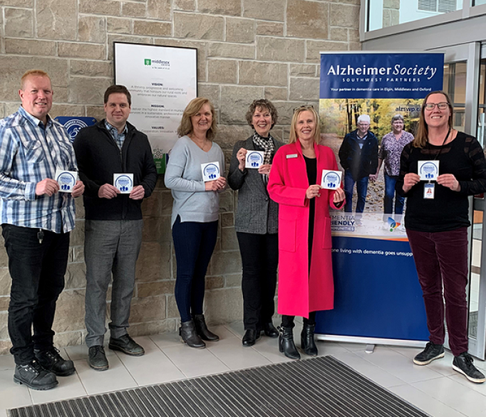 Justin Fidler, Lise Massen, Sean Hanlon and Mayor Aina DeViet of Middlesex Centre, and Leslie Rand and Susan Oster from the Alzheimer Society Southwest Partners, hold the new Dementia Friendly Community Supporter decals that will be going up at municipal buildings.